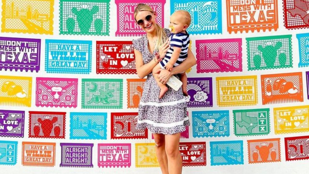 Kelsey, an Austin, TX influencer, and her son smiling in front of a wall decorated with various Austin-themed signs.