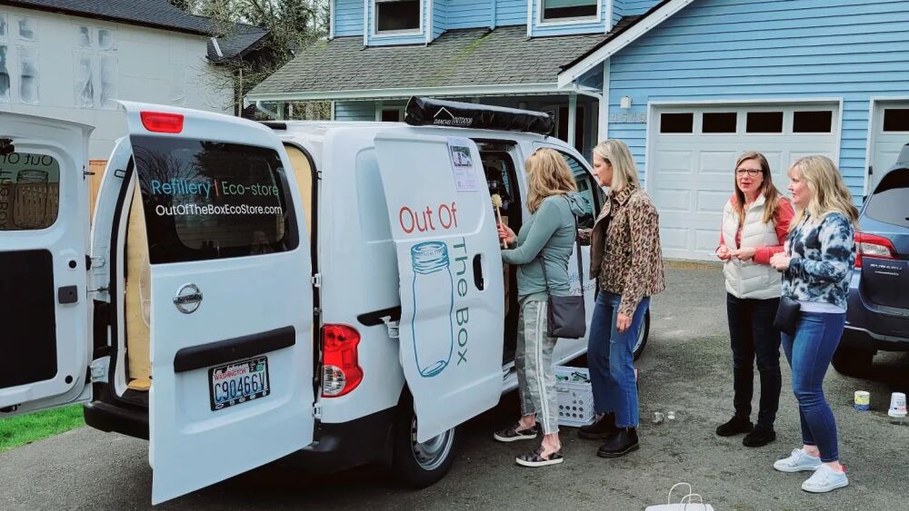 A group of women huddle around Out of the Box Eco Store's mobile refillery in a residential driveway.