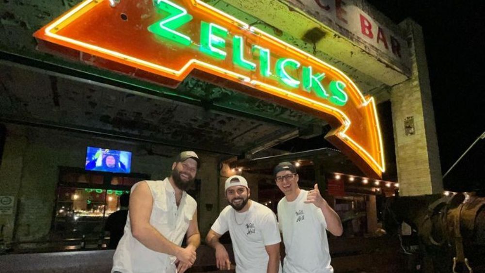 Three friends smiling and posing under the Zelick's Bar sign in San Marcos, Texas.