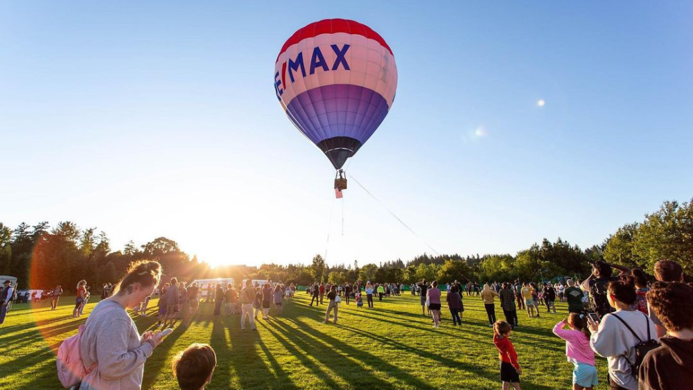 A red, white and blue hot air balloon rises in the morning sky just above a crowd of people