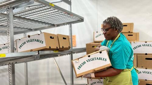 A woman with an apron moving a box of fresh vegetables