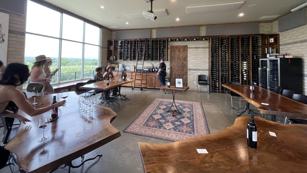 A room with curved tables and a rug in the floor, and wine bottles lining the walls.