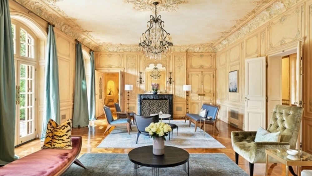 A sitting room with plenty of tables and chairs, a vase with flowers, and a chandelier. 