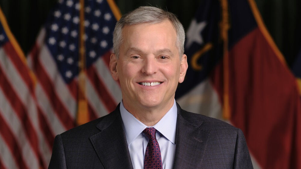 A portrait photo of North Carolina Governor Josh Stein in a black suit in front of the American flag.