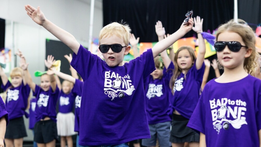 Photo of kids all wearing purple t-shirts and raising their hands in the air. 