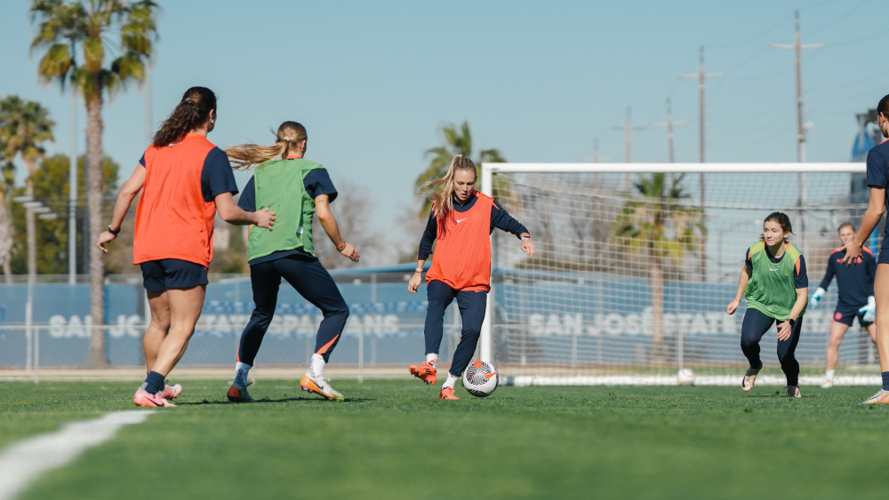 Soccer players from Bay FC kick around a soccer ball on lush green fields in San Jose during practice.
