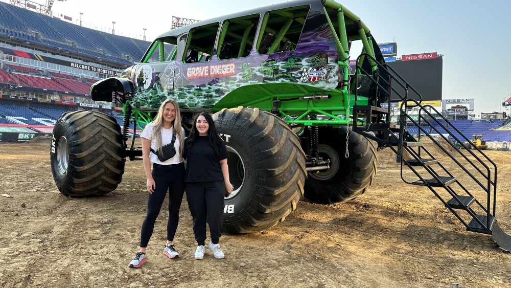 City Editors Skylar and Dylan stand in front of a green and purple monster truck at Nissan Stadium.