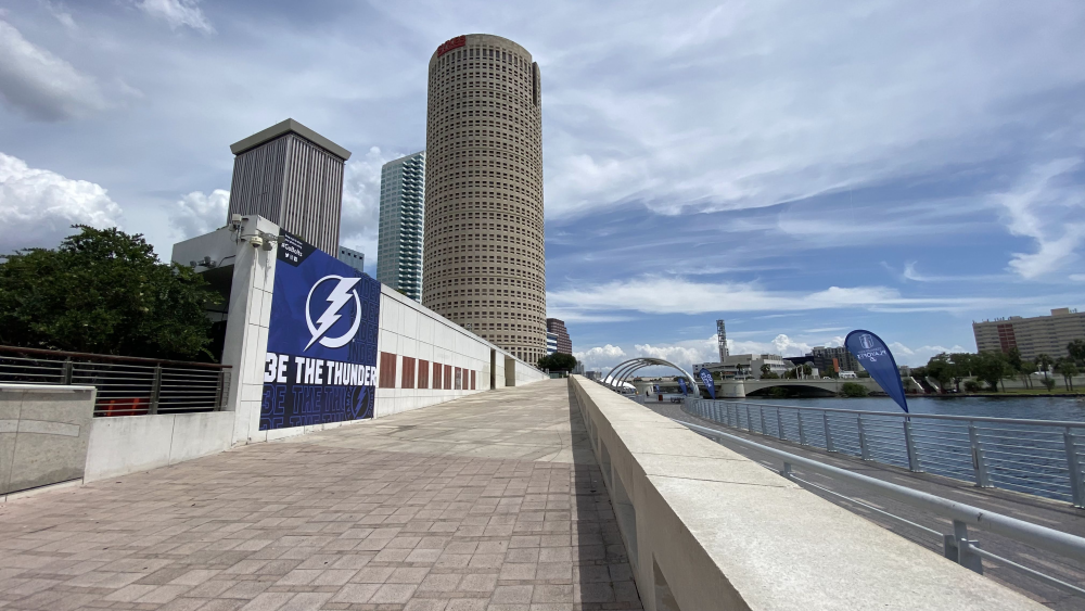 The Rivergate Tower along the Tampa Riverwalk. There is a flag for the Tampa Bay Lightning in the foreground which reads "Be the Thunder", and the Hillsborough River runs along the right side of the photo.