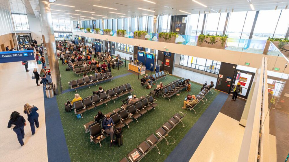 Travelers sit in seats next to large windows in Concourse B at Portland International Airport