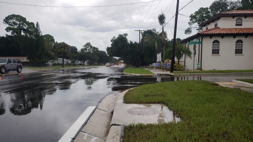 A photo of Mannatan Ave and Vasconia Street with flooding on the roads. The residential area has houses around and there are cars driving through the water nearby.