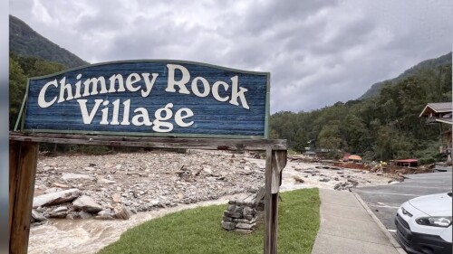 The village sign of Chimney Rock with widespread storm damage in the background.