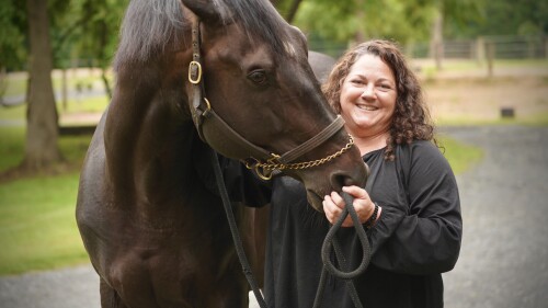 A woman poses for a photo while holding the halter to a horse.