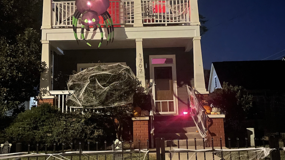Home decorated for Halloween with spider webs on the gate and a giant spider hanging from the roof.