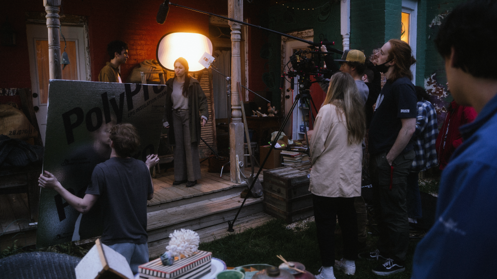 People standing around a front porch with filming equipment.