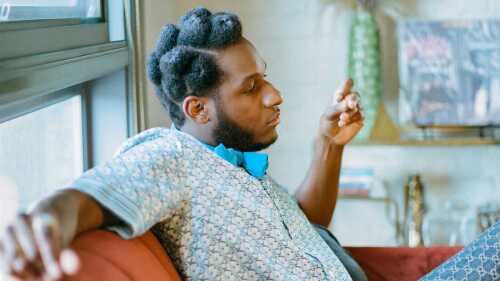 Singer Leon Bridges sits on an orange couch.