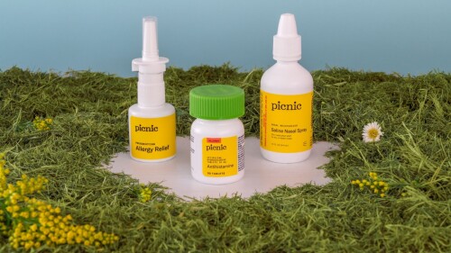 A collection of three bottles of allergy medications sitting in a field of ragweed and grass.