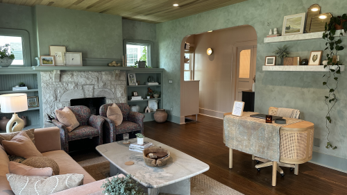 The check-in area, which features an arched doorway, desk setup, marble coffee table, pink couch, two vintage patterned chairs, and a stone fireplace.