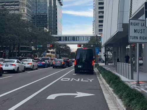Cars line up in downtown Tampa. They are at a red light and surrounded by skyscrapers.