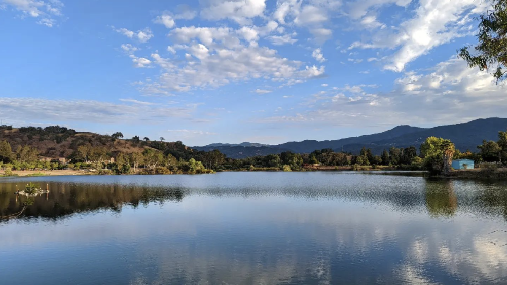 A lake with mountains in the background and a blue sky with a few white clouds.