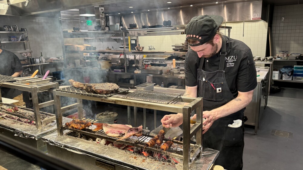 A chef tends to meat grilling in the kitchen of a restaurant.