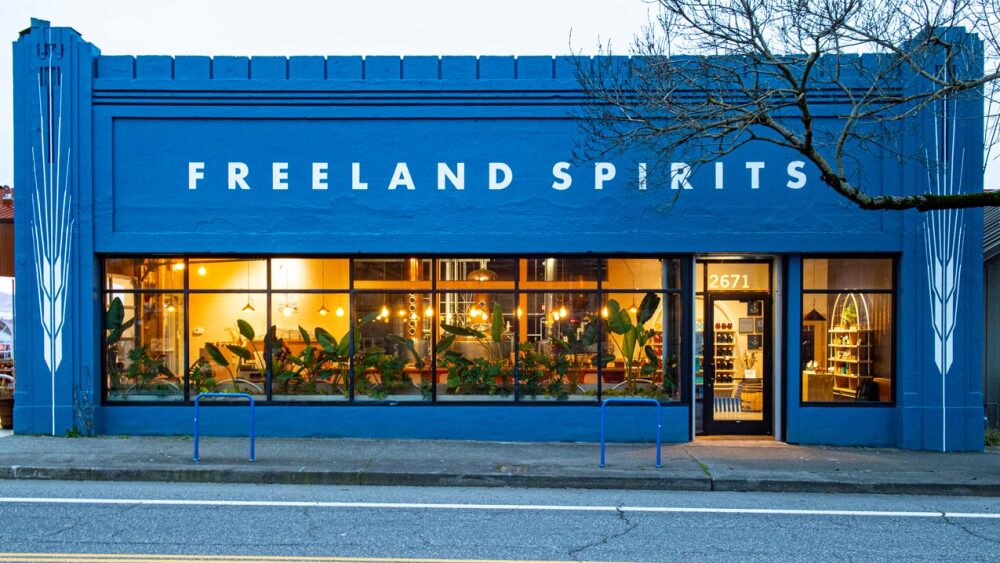 A blue building at says Freeland Spirits, through the windows a soft orange glow can be seen