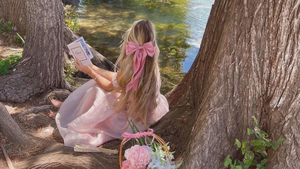 Austin-based influencer Rachel poses in a pink dress with a book near a pond.