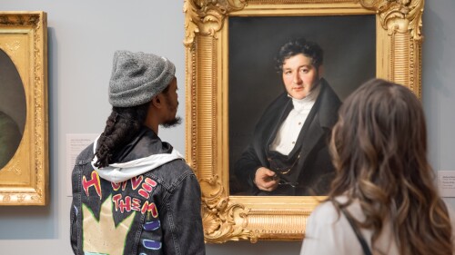 Visitors at Portland Art Museum get an up close look at an oil painting portrait of a man in a suit holding spectacles.