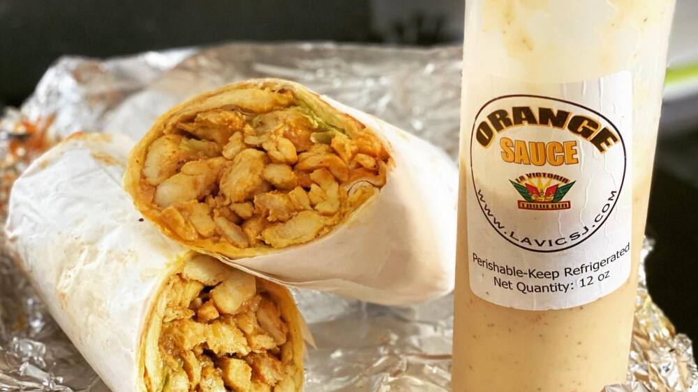 A cut and displayed burrito and a squeeze bottle of orange sauce.