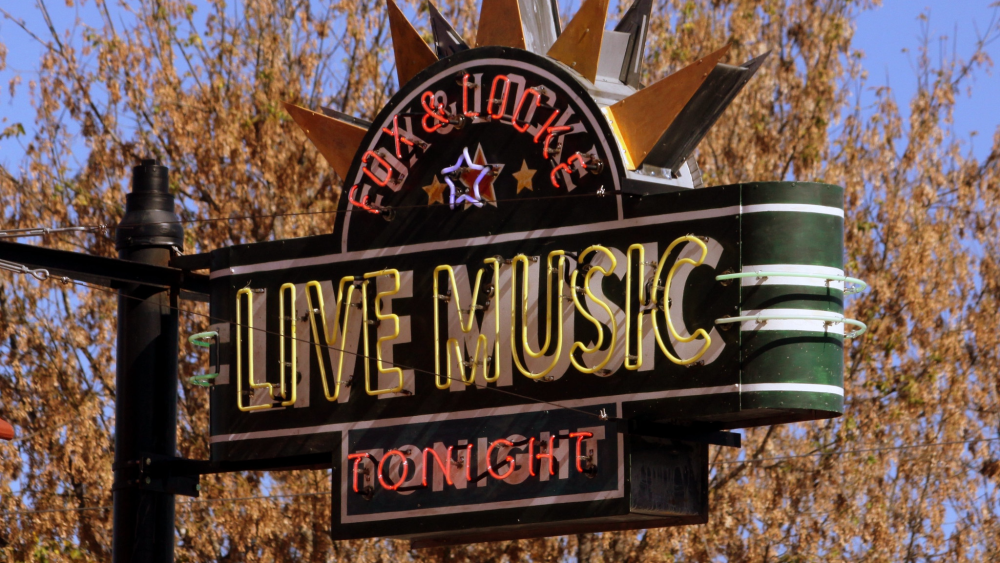 An up-close perspective of a neon sign reading "Fox & Locke Live Music Tonight" and a tree with orange leaves in the background.
