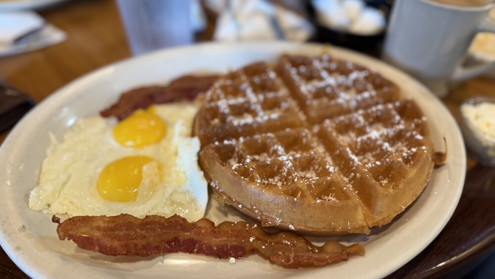 A plate of eggs, bacon, and waffles is served on a plate.
