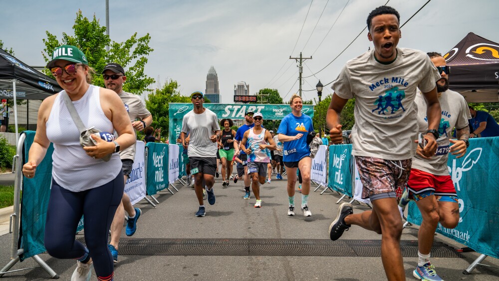 Runners enthusiastically cross a race finish line with the Uptown skyline in the background.