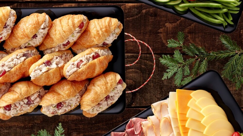 A vegetable tray, meat and cheese tray, and sandwich tray with chicken salad croissants