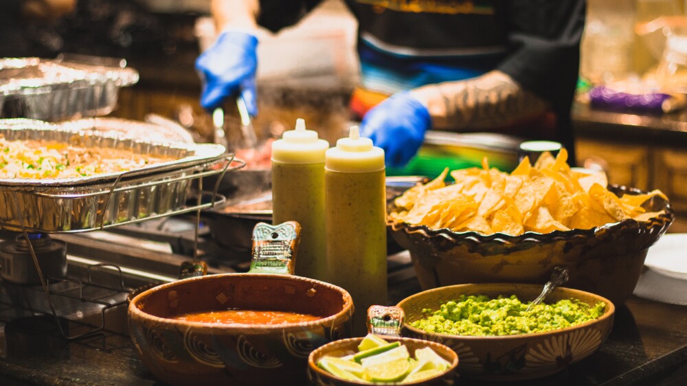 Candles and plated food surround a paper menu clipped to a wooden slab.