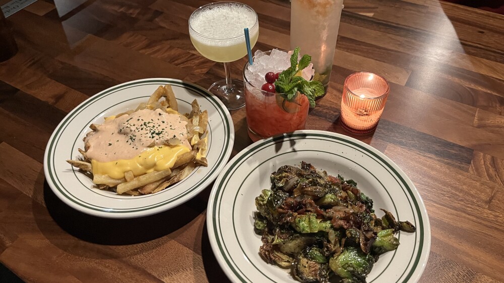 A plate of Brussel sprouts, a plate of animal fries, and three cocktails at Gussie's.