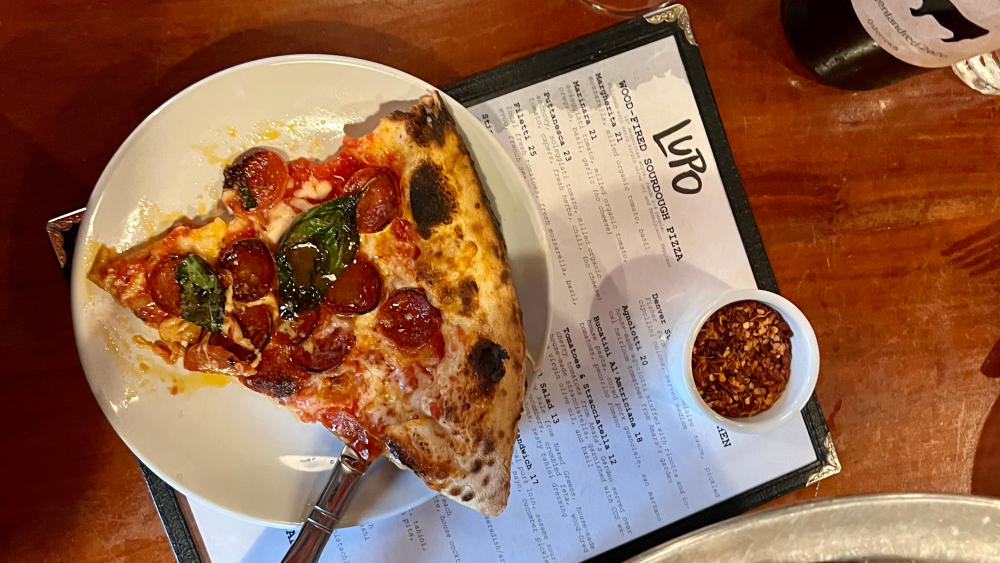 A slice of pizza on a plate sitting on a menu for Pizza Lupo