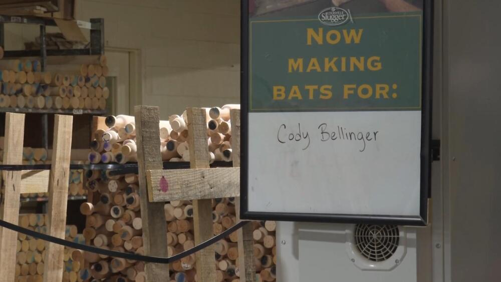 A stack of baseball bat barrels sit in shelves behind a sign reading "Now making bats for: Cody Bellinger"