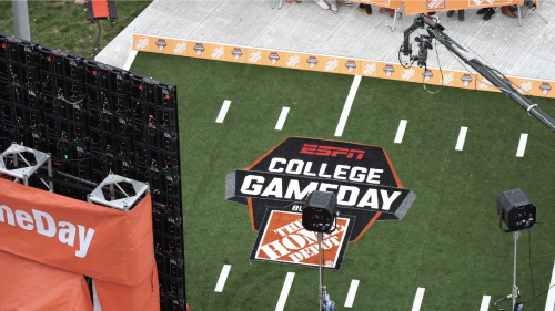A camera setup and lighting equipment surround the ESPN “College GameDay Built by The Home Depot” logo painted on artificial turf resembling a football field, seen from an overhead angle.