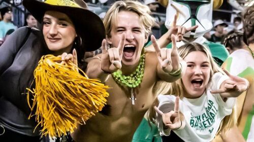 USF Bulls fans celebrate in the stands at Raymond James Stadium. They are dressed in green and gold and are making the Bulls hand signal.