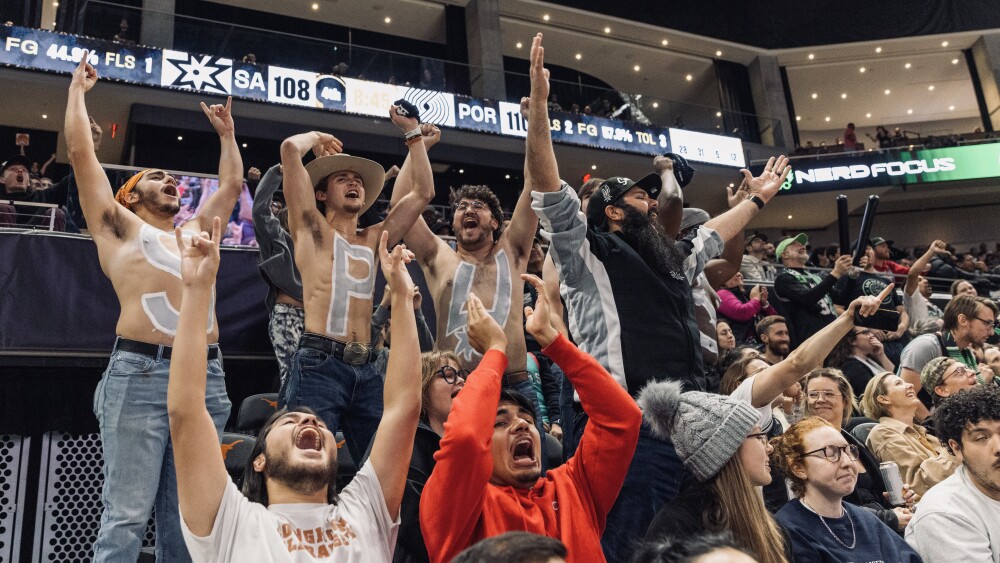 A group of men spelling out "Spurs" with silver paint on their chests.