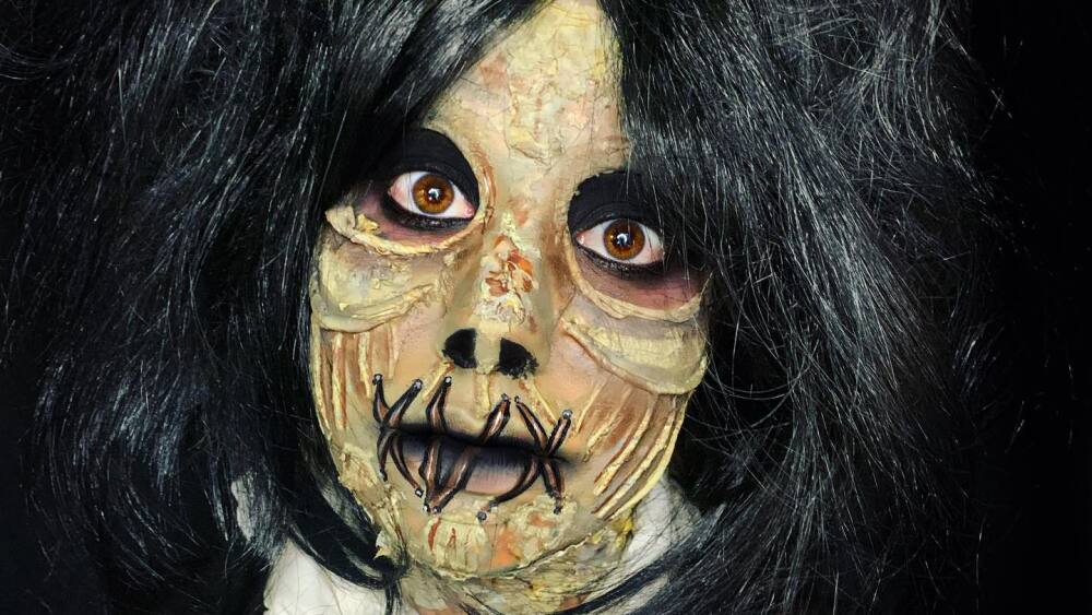 A female character with petrified skin, black hair, and lips sewn together