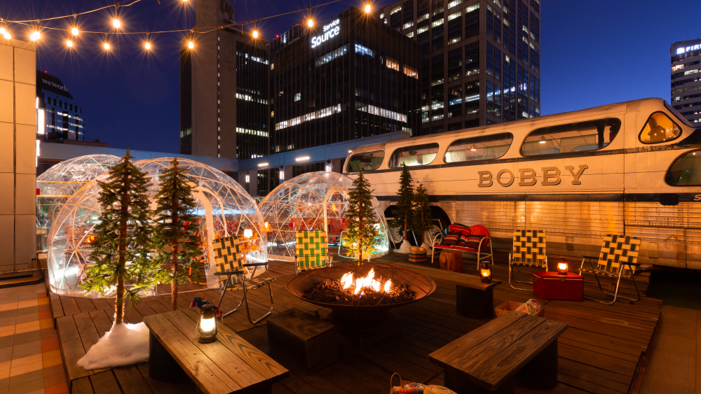 A rooftop space filled with a firepit, artificial trees, igloos, and a retro bus