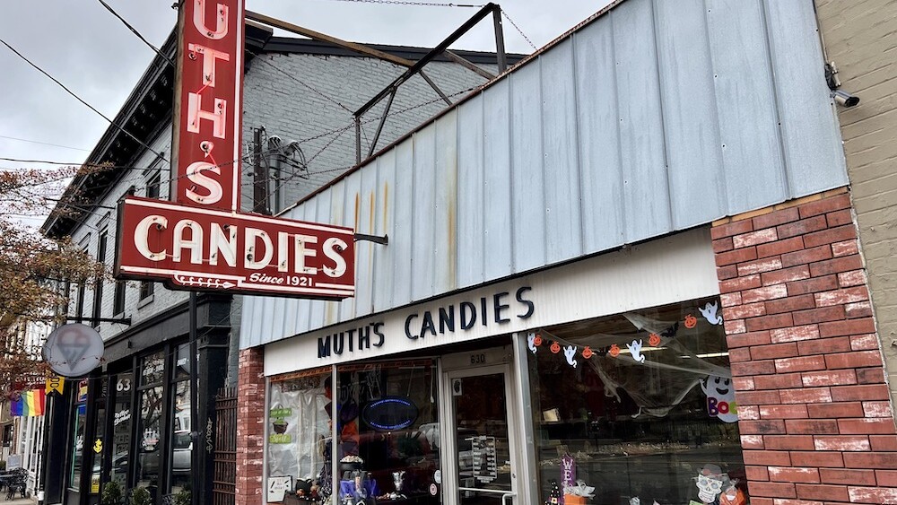 Store front of a candy store with class windows and red sign.