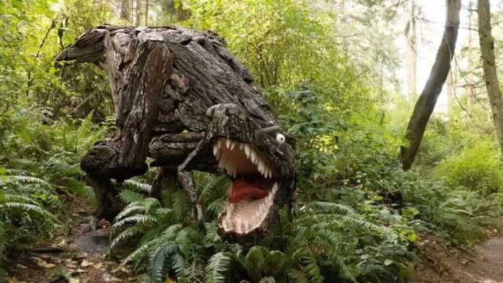 A dinosaur sculpture peaks out from the woods.