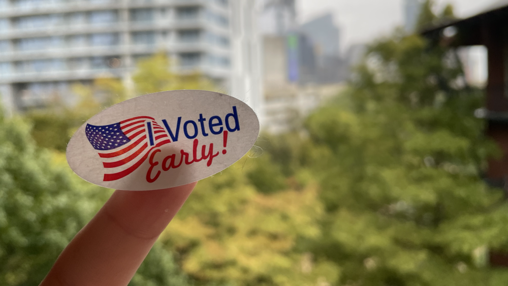 An "I voted early" sticker on a finger in front of a green background.