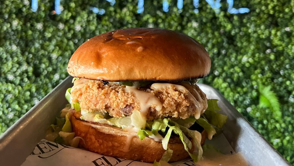 A vegan chicken sandwich in front of a sign that reads "I licked it so it's mine."