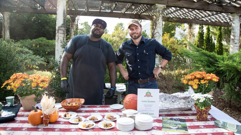 A chef and a farmer pose for a photo behind a picnic table of food.