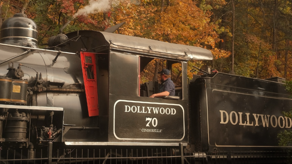 The front side of the train at Dollywood as it moves along the tracks. Fall trees in orange hues can be seen behind it.