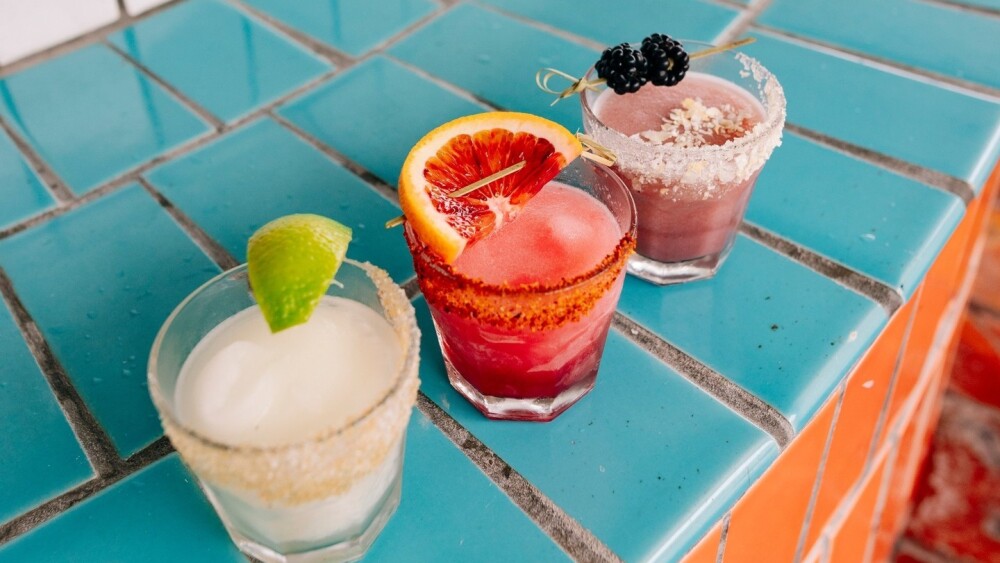 Three margaritas in glasses on a tiled ledge.