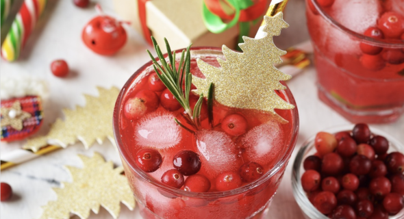 A holiday cocktail topped with cranberries and a sprig of rosemary