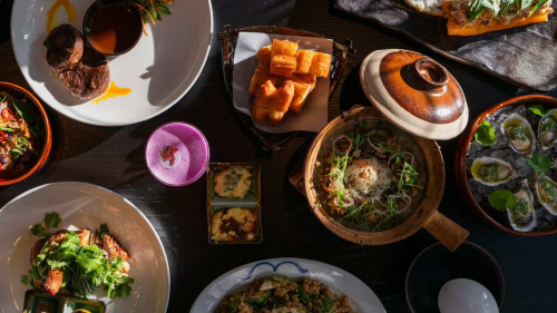 A spread of Chinese-Vietnamese dishes featuring green, tan, and yellow colors. There are scallops to the right and a purple cocktail to the left.